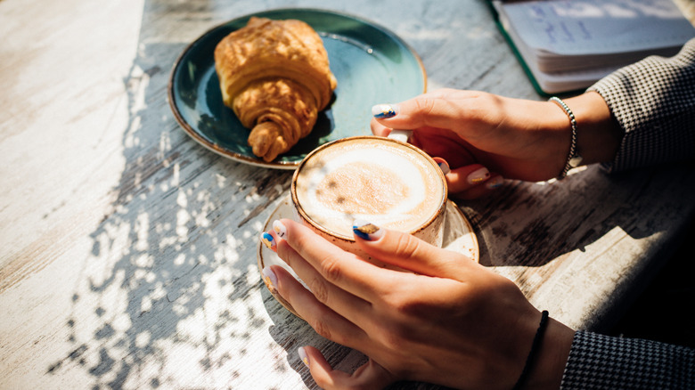 Coffee cup and croissant on sunny table