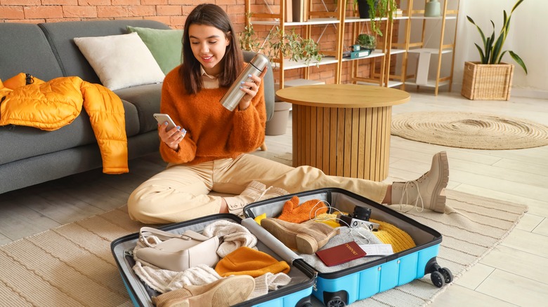 Woman holding bottle, packing suitcase