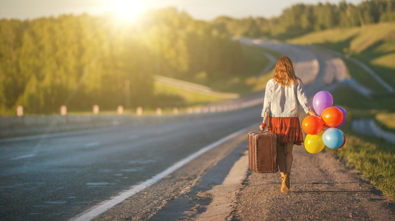 Woman walking down road holding suitcase and balloons