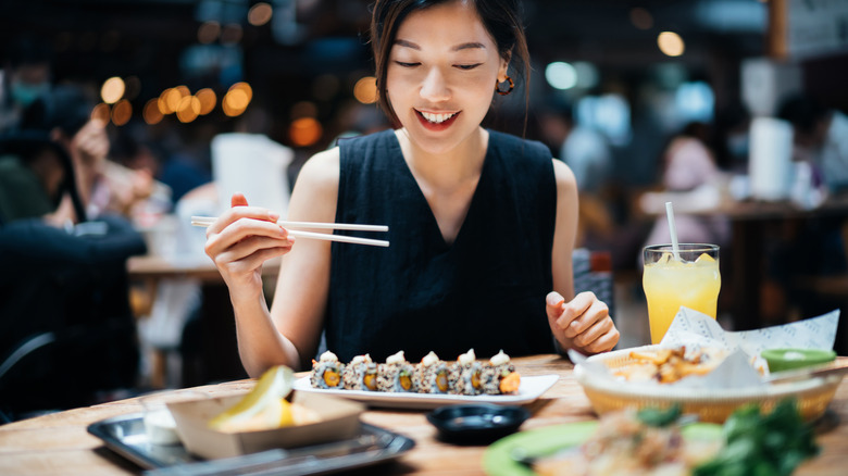 A woman preps her chopsticks to eat a roll of sushi