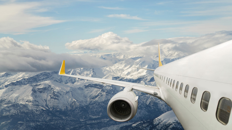 A plane flies over snow-capped mountains.