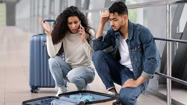 Woman on phone and man with hand to head over suitcase