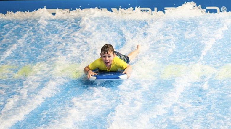 A smiling child rides a FlowRider.