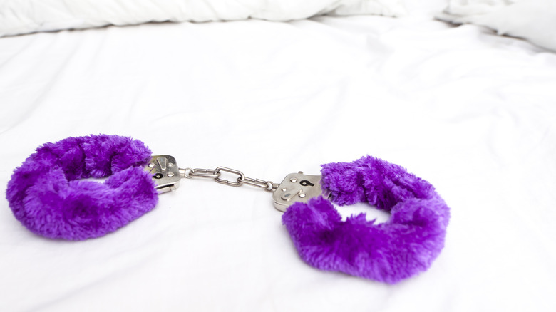 Fuzzy purple handcuffs on bed