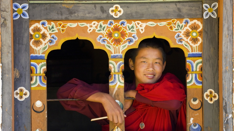 Smiling monk looking out ornate window, Bhutan