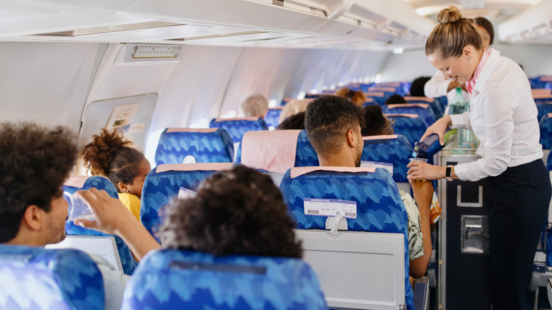 Flight attendant pours a drink for passenger