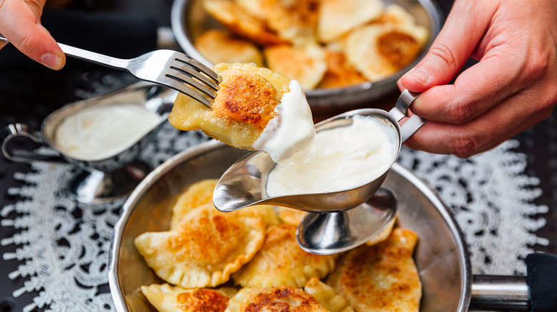 Person dipping a pierogi into sour cream