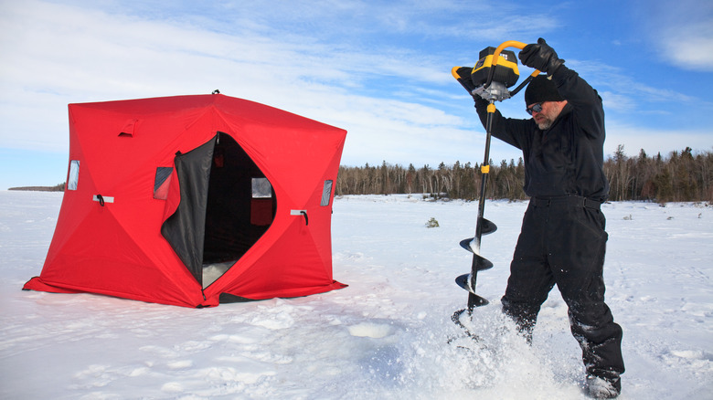 A man drills an ice fishing hole on a frozen lake