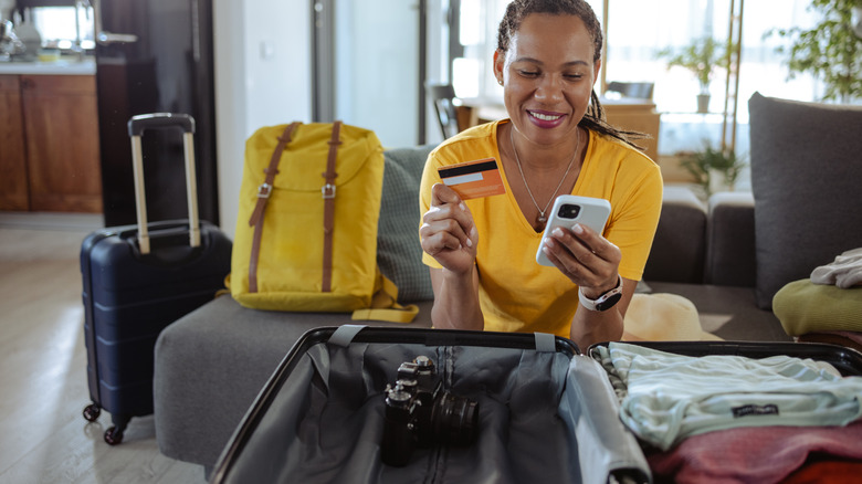 Traveler sitting by suitcase paying with credit card