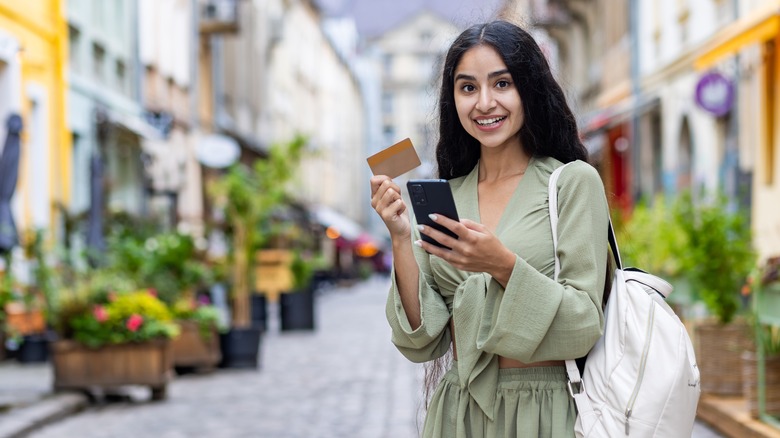 Young traveler standing outside holding a credit card