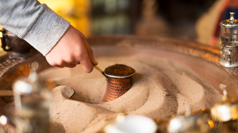 Hand warming Turkish coffee on sand
