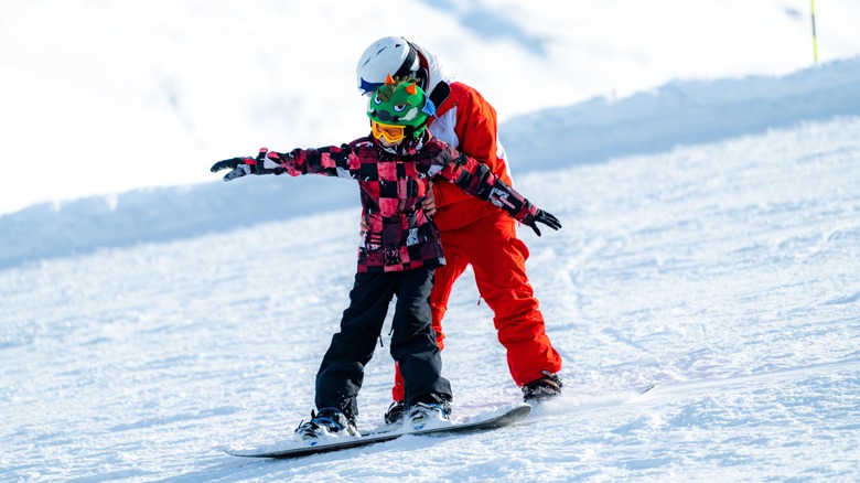 Instructor teaching child to snowboard