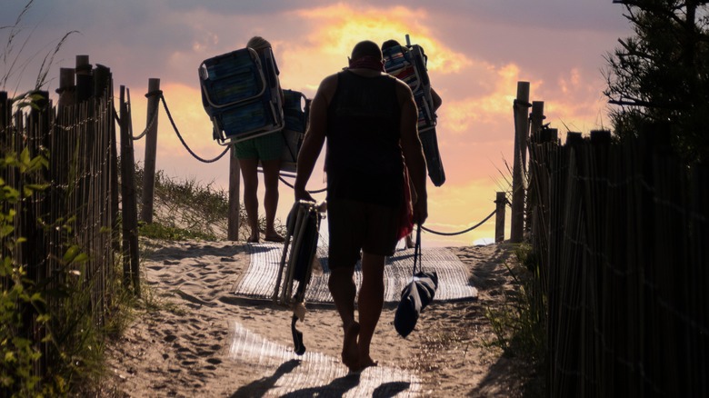 Three people walking to Bethany Beach with chairs at sunrise