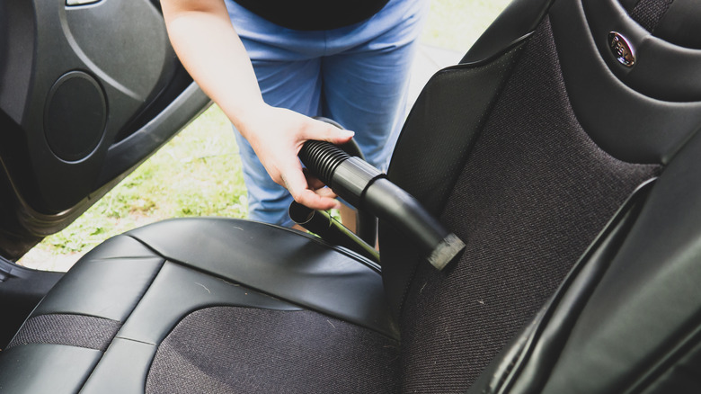 person vacuuming back seat of car