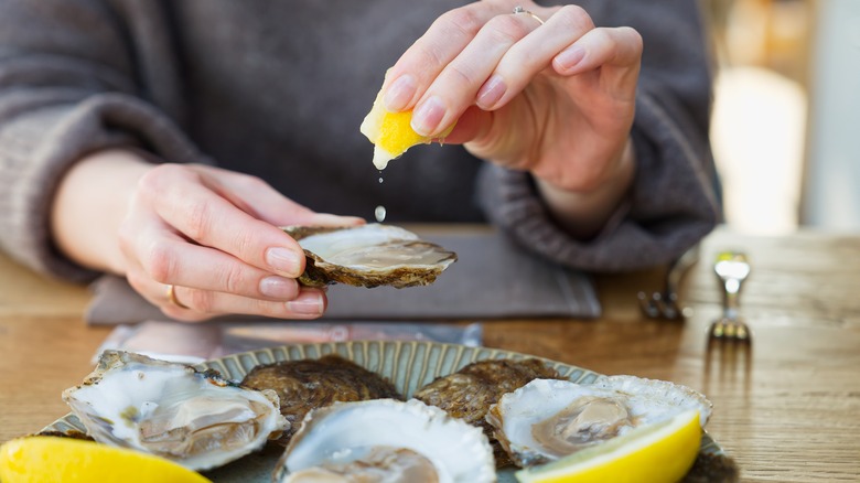 Hand squeezing lemon onto oysters