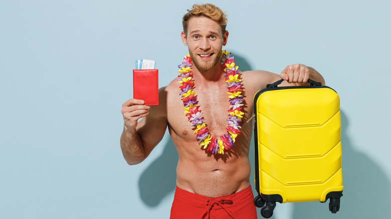 A shirtless man wearing a lei holds a suitcase and boarding pass.