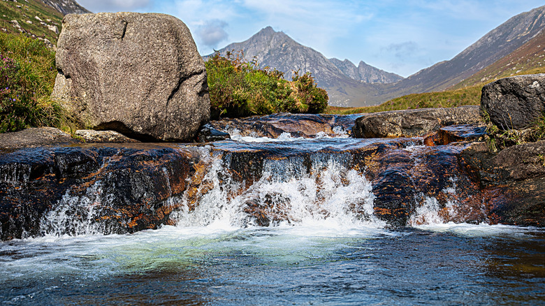 A waterfall drops into a swimming hole with mountains in the distance