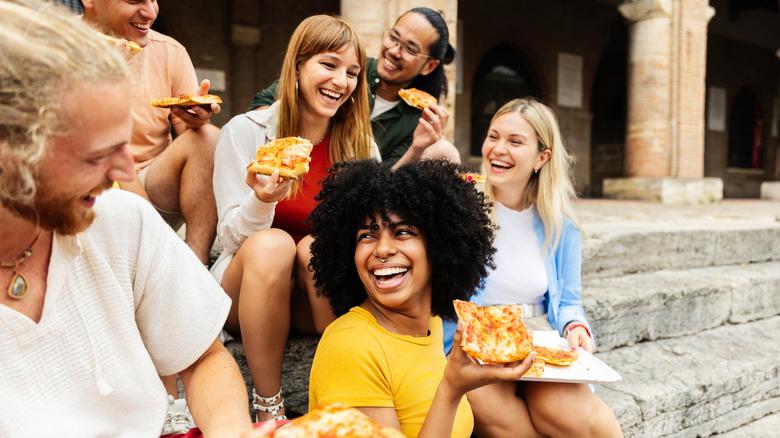 A group of young people eating pizza on stairs in Italy