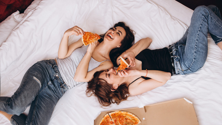Friends eating pizza in bed