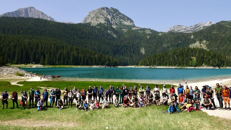 Large group of hikers posing for a portrait in front of a lake and mountains.