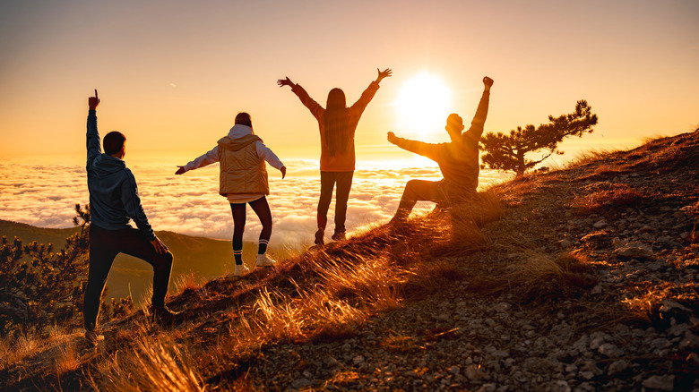 Hikers celebrate on mountaintop, silhouetted in front of a sunset.