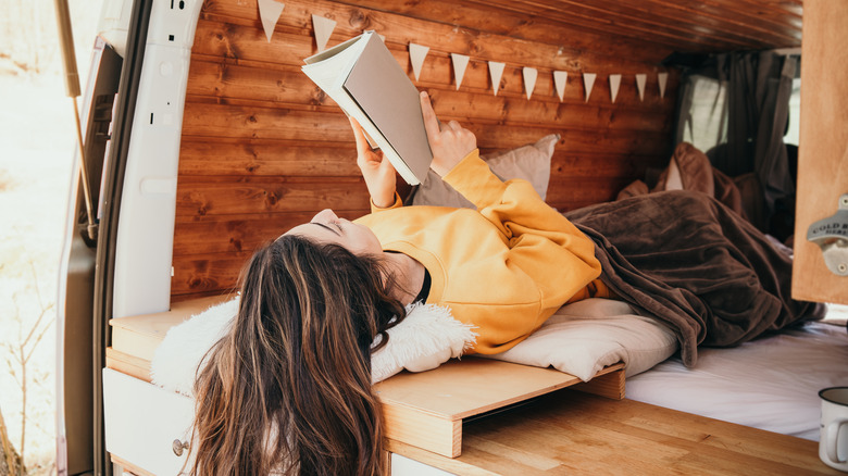 Woman relaxes and reads in a custom camper van