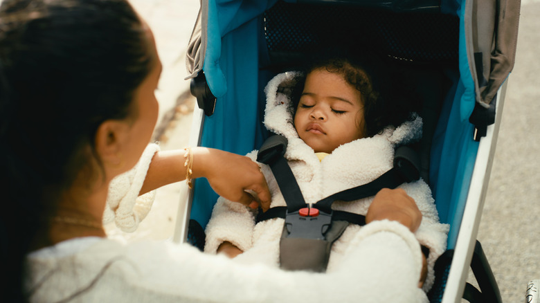 Nanny tucking baby into stroller