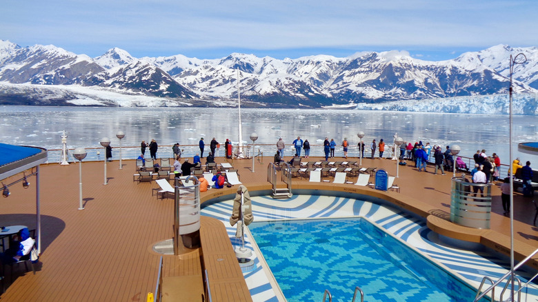 People standing on cruise ship railing, near pool, overlooking glaciers