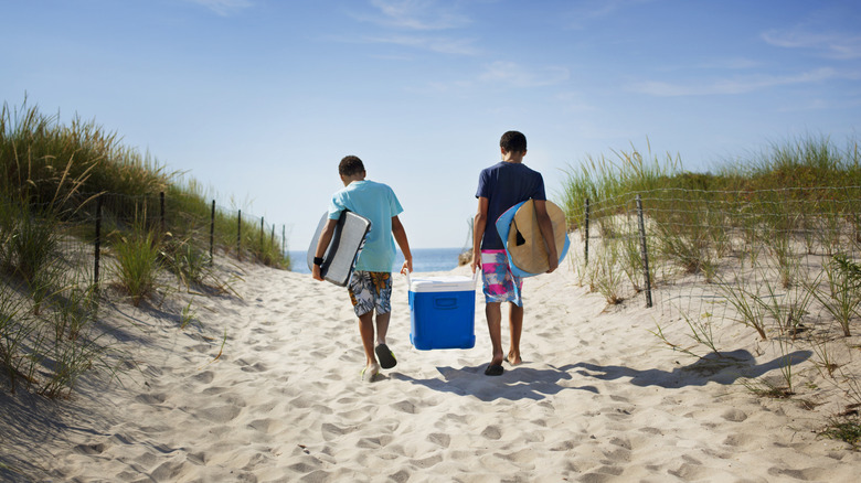 Two people carrying a cooler on the beach