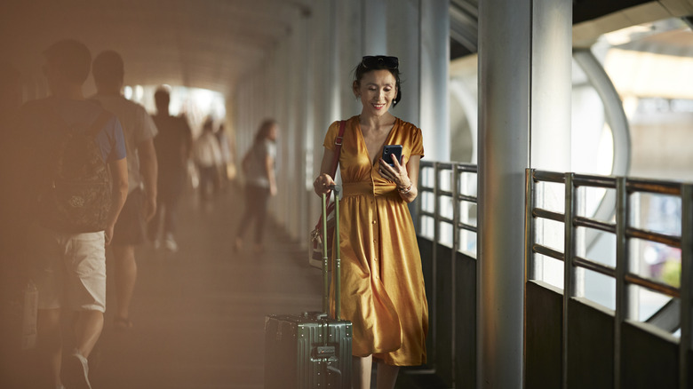 Traveler rolling suitcase and using smartphone