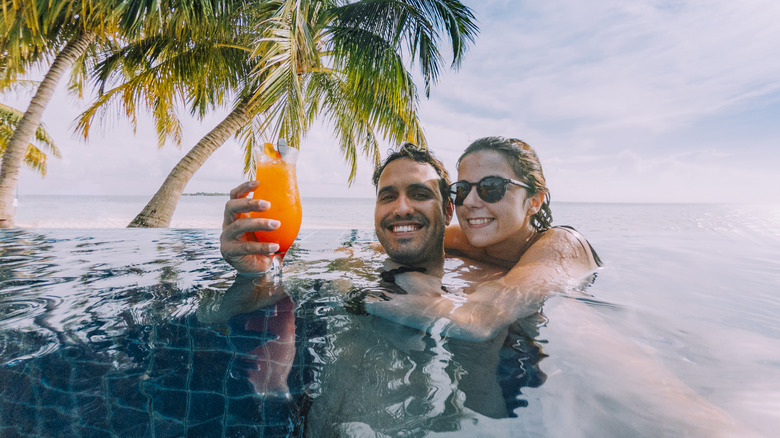 A couple drinks a cocktail in a pool.