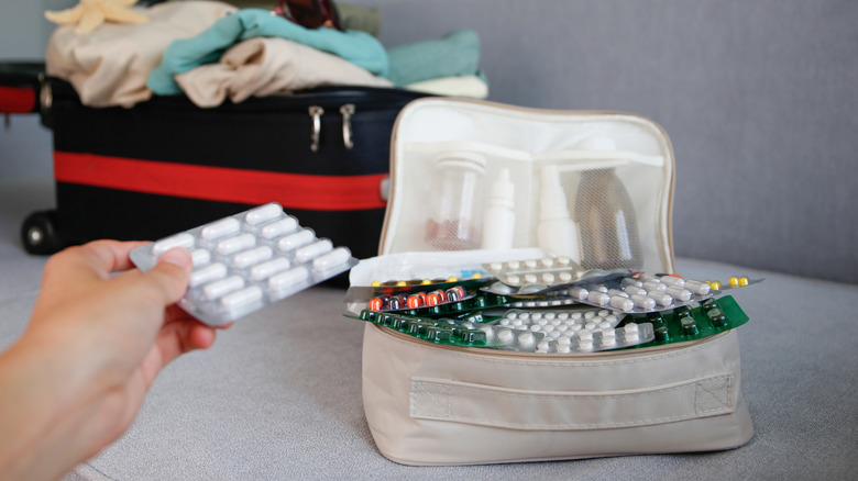 Hand holding blister pack next to a bag of medication and open luggage