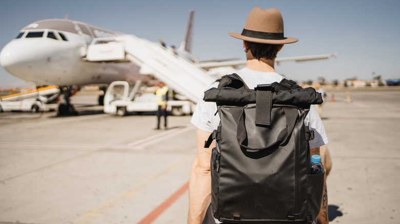 Man with a hat and backpack walking toward plane