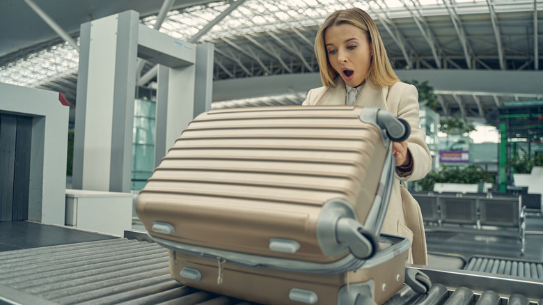 Shocked woman looks into suitcase on conveyor belt