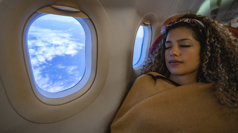 plane passenger covered with blanket sleeping by window