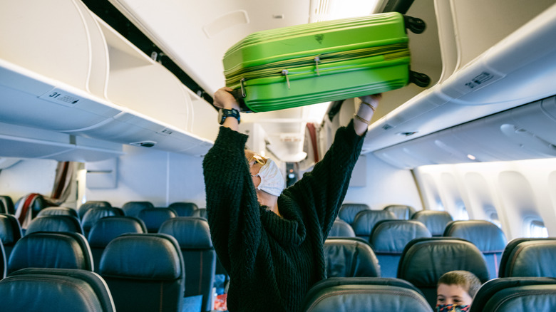 person putting luggage in overhead compartment