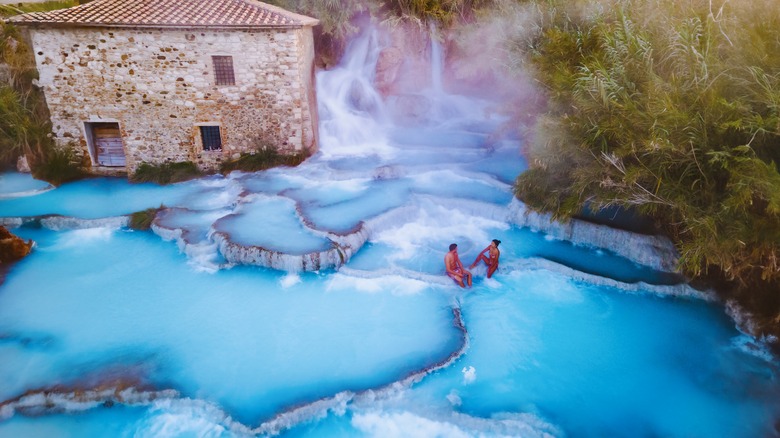 Two people sit near the waterfalls in Italy's Saturnia Hot Springs