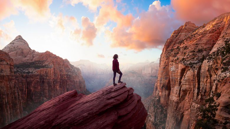 Woman standing on a rock watching sunset over canyon