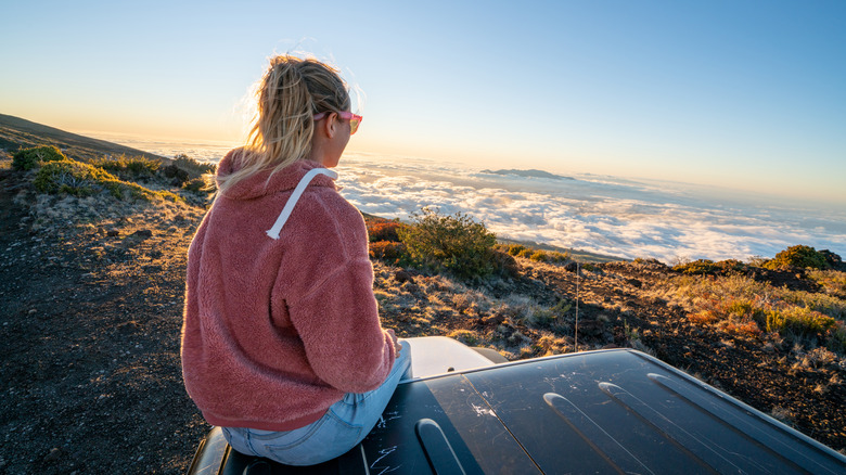 Woman sitting on top of car watching cloud coverage over Hawaiian volcano