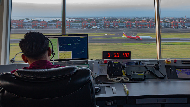 air traffic controller with headset at control panel with plane on runway in distance