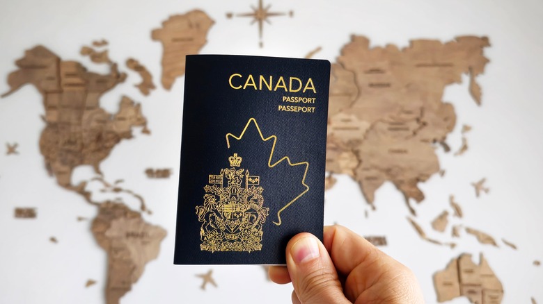 hand holding a Canada passport with a world map behind