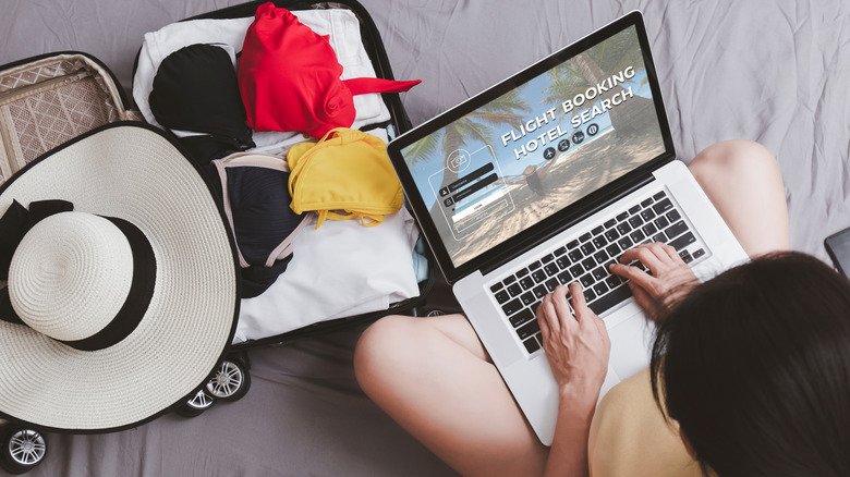 Woman booking travel on laptop with packed suitcase