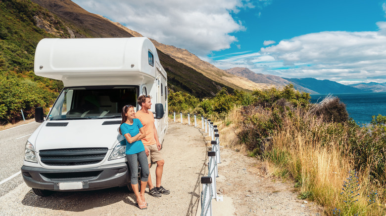 couple sitting against parked RV