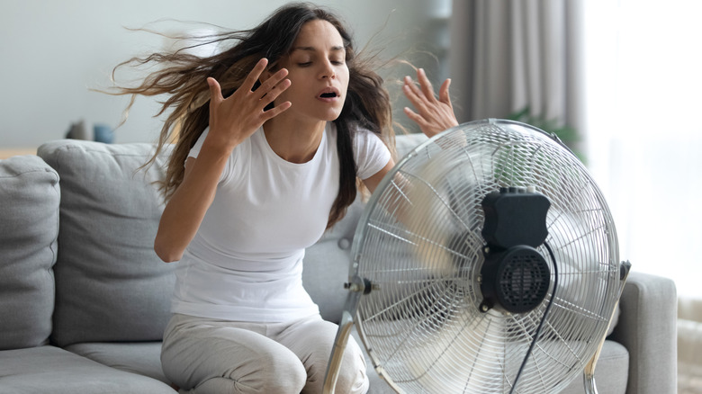 A woman sits in front of an electric fan to cool down.