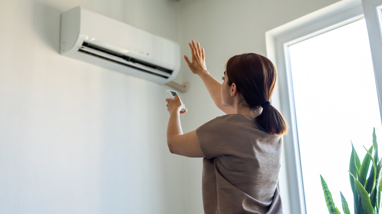 A woman checks to see if cool air is coming out of the AC unit.