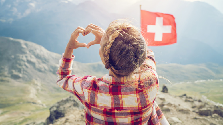 Swiss woman making heart gesture with the Swiss flag in the background