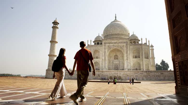 A couple holds hands in front of the Taj Mahal