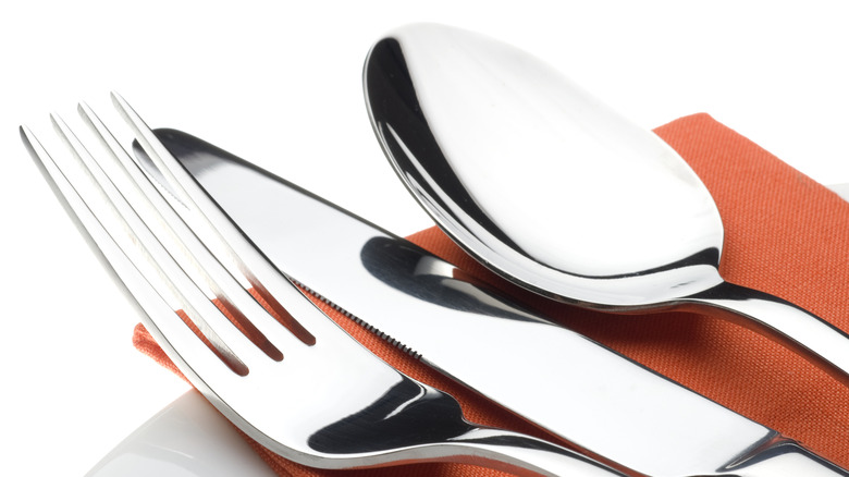 A shiny fork, knife, and spoon sit on a napkin