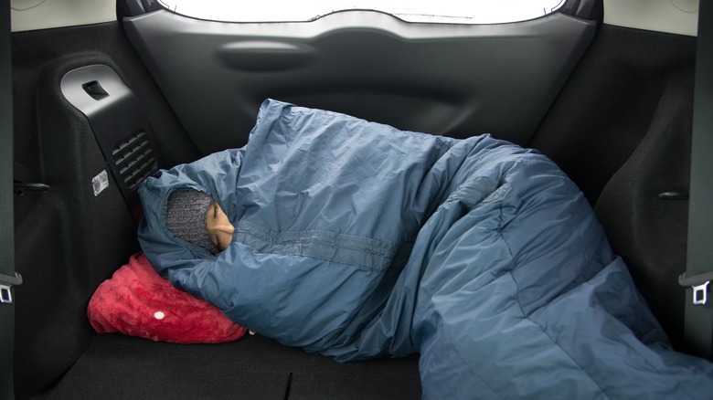 man in sleeping bag in car