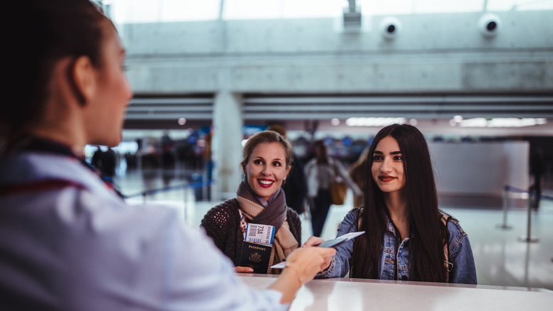 Flight attendant handing two women their tickets at the airport